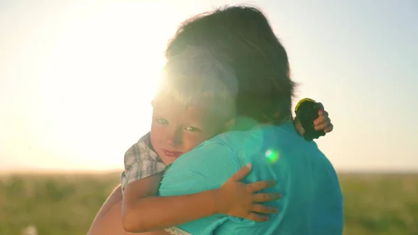 快乐的儿子在夏日的阳光下抱着妈妈.可爱亲切的小男孩抱着一位善良的母亲。可爱的小儿子拥抱妈妈，享受家庭的幸福。在大自然中行走的家庭 — 图库照片
