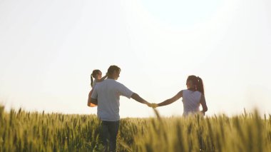 Baba, çocuk ve anne, el ele yürüyün. Sağlıklı anne, baba ve küçük kız birlikte doğanın tadını çıkarıyorlar. Çocuklu mutlu çiftçi ailesi buğday tarlasında yürüyor. Yavaş çekim.