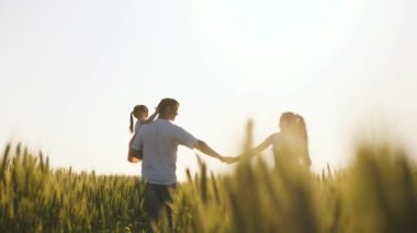 Baba, çocuk ve anne, el ele yürüyün. Sağlıklı anne, baba ve küçük kız birlikte doğanın tadını çıkarıyorlar. Çocuklu mutlu çiftçi ailesi buğday tarlasında yürüyor. Yavaş çekim.