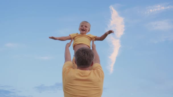 Papá lanza a su hijo feliz al cielo azul. Padre e hijo jugando en el parque, riéndose y abrazándose juntos. Feliz viaje en familia. El bebé está en brazos de los padres. Papá está fuera. Concepto de familia feliz — Vídeo de stock