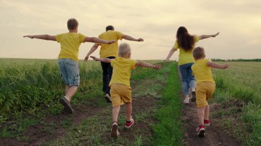 Mutlu aile takımı, sahada birlikte koşuyorlar, mutlu bir şekilde ellerini sallıyorlar. Oğullar, çocuklar, anne, baba koşun, oynayın, sevinin, yazın doğanın tadını çıkarın. Aile takım çalışması. Farklı yaşlarda bir grup insan
