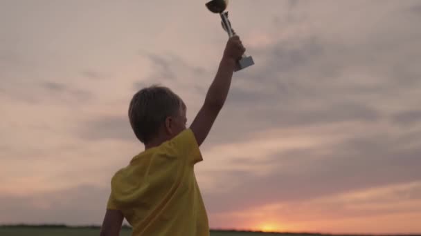 A child athlete celebrates his victory, joyfully raises his hands with a cup and jumps happily. The concept of winning sports in business and in life. Be winner and champion everywhere from childhood. — Stockvideo