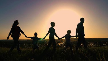 Siluet, mutlu aile takımı güneşin altında el ele yürüyorlar. Mutlu çocuklar, oğullar, anne ve babayı ellerinizle tutun. Ekip çalışması. Gün batımında farklı yaşlarda bir grup insan. Mutlu aile oyunu