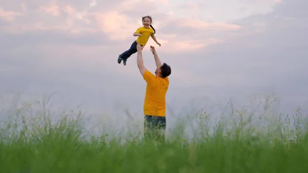 Father and little child play, laugh and hug together. Dad throws his happy daughter into blue sky in summer park. Dad day off. Happy family travels. Baby in arms of parent. Happy family — Zdjęcie stockowe