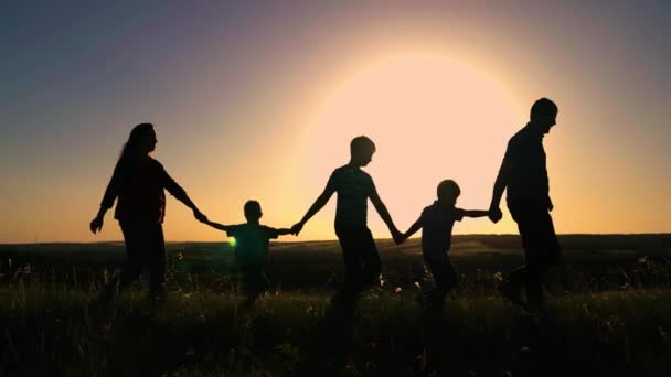 Silhouette, happy family team walking together holding hands in sun. Happy children, sons, hold mom, dad by hand. Teamwork of people. Group of people of different ages at sunset. Happy family playing — Stock video