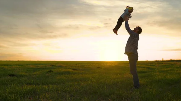 Bambino in braccio ai genitori. Papà getta la sua figlia felice nel cielo blu in raggi di sole. Padre e bambino giocano, ridono e si abbracciano insieme. Buon viaggio in famiglia. Il giorno libero di papà. Concetto di famiglia felice — Foto Stock