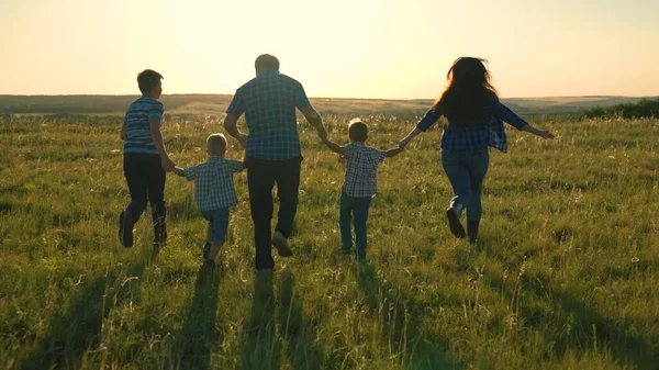 Glad familj team, springa tillsammans hålla händerna i parken. Lyckliga söner, barn, mamma och pappa springer, leker, gläds, njuter av naturen på sommaren. Lagarbete av människor. En grupp människor i olika åldrar vid solnedgången. — Stockfoto