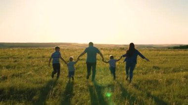 Mutlu aile takımı, parkta el ele koşun. Mutlu oğullar, çocuklar, anne ve baba koşar, oynar, eğlenir, yazın doğanın tadını çıkarırlar. Ekip çalışması. Gün batımında farklı yaşlarda bir grup insan.