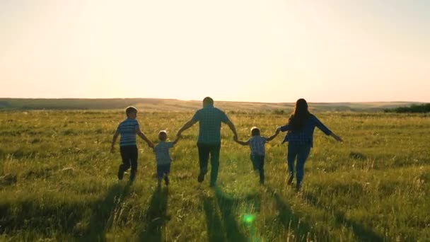 Glückliches Familienteam, das Hand in Hand im Park läuft. Glückliche Söhne, Kinder, Mama und Papa rennen, spielen, freuen sich, genießen die Natur im Sommer. Teamarbeit der Menschen. Eine Gruppe von Menschen unterschiedlichen Alters bei Sonnenuntergang. — Stockvideo