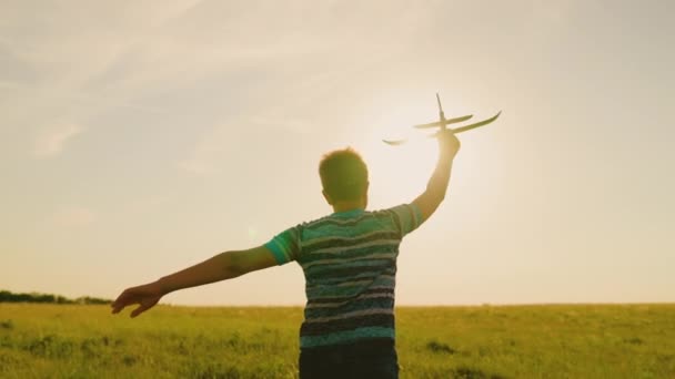 Niño, niño corre con avión de juguete en el campo de verano en los rayos de la puesta del sol. Niño feliz corriendo en el parque, jugando con el avión de juguete en la naturaleza. Familia feliz. Chico sueña con volar. Niño despreocupado jugando al aire libre — Vídeo de stock