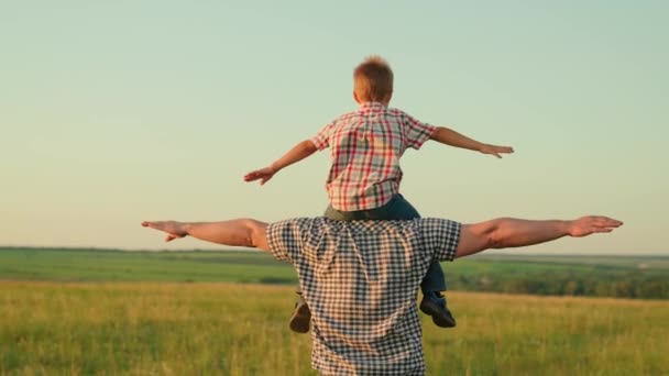 Papà cammina con il bambino sulle spalle, alza le braccia e vola come un aereo. Papà gioca con suo figlio, portato sulle spalle del suo amato bambino in estate sul campo. Famiglia felice sta giocando nel parco. — Video Stock