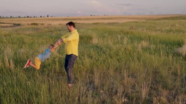 Babam mutlu oğlunun kollarında gün ışığında parkta dolaşıyor. Baba ve küçük çocuk birlikte oynar, güler ve sevinir. İyi yolculuklar. Bebek ebeveynlerin kollarında. Babalar izinli. Mutlu aile kavramı