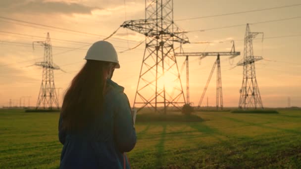 Een elektrotechnicus, een vrouw die met een tablet werkt, werkt met elektriciteit naast een elektrische toren. Industrie van energie bedrijfstechnologieën. Een elektrotechnicus werkt op digitale tablet — Stockvideo