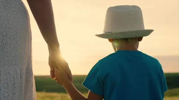 Bonne promenade en famille, gamin, garçon, maman à l'extérieur. Bonne enfance familiale. Maman, fils marchent ensemble en se tenant la main au soleil. Dans la main des enfants est spinner jouet. Des gens dans le parc. Parents, enfants joyeux, rêve — Photo