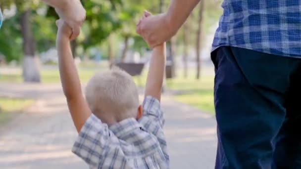 Tato, synu, mama bawi się w parku miejskim, szczęśliwe dziecko trzyma się za ręce rodziców i skacze. Praca zespołowa. Szczęśliwa rodzina biegnie w parku na ulicy, trzymając się za ręce wiosną, latem. Szczęśliwego zdrowego dzieciństwa — Wideo stockowe