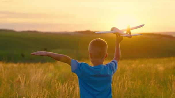 Szczęśliwy dzieciak biegający w parku, bawiący się zabawkowym samolotem w naturze. Chłopak marzy o lataniu. Beztroskie dziecko bawiące się na zewnątrz. Dziecko, chłopiec biega z zabawkowym samolotem na letnim polu w promieniach zachodzącego słońca. Szczęśliwa rodzina — Wideo stockowe