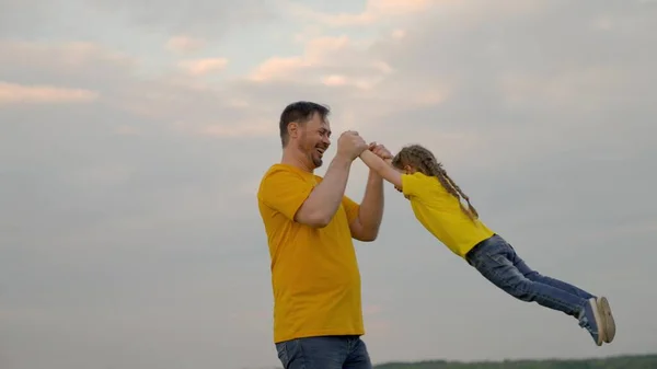 Tata się bawi, okrąża swoją szczęśliwą córkę dłońmi przed niebem w letnim parku. Ojciec i małe dziecko radują się, śmieją i przytulają razem. Szczęśliwej rodzinnej podróży. Dziecko jest w ramionach rodziców. Szczęśliwa rodzina — Zdjęcie stockowe