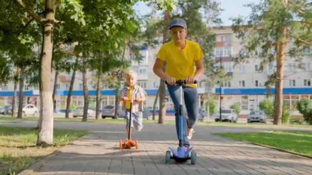 Děti, synku, chlapci jezdí na skútru společně pod širým nebem. Šťastné roztomilé děti hrát v parku na ulici, naučit se rovnováhu na skútru. Chlapci si hrají bezstarostně v dětském parku. Rodinný letní víkend — Stock video