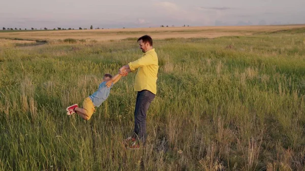 Pappa cirklar runt armarna på sin lyckliga son i parken i solsken. Far, lilla barn leker, skrattar och gläds tillsammans. Trevlig familjeresa. Barnet är i föräldrarnas famn. Pappor ledigt idag. Lyckligt familjebegrepp — Stockfoto