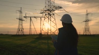 Bir elektrik mühendisi dijital tablet üzerinde çalışır. Elektrik mühendisi, bilgisayar tabletinde çalışan bir kadın, elektrik kulesinin yanında çalışıyor. Enerji iş teknolojileri endüstrisi.