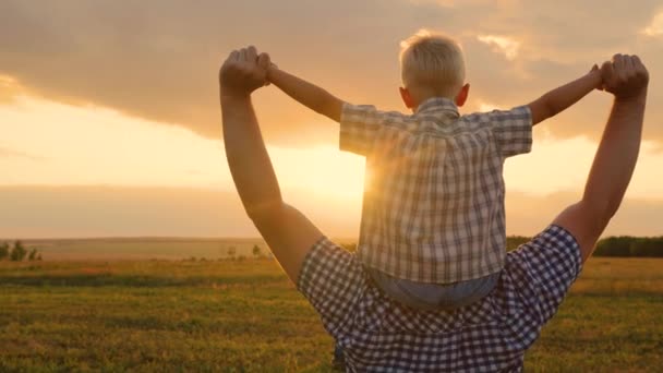 Famiglia felice che riposa al parco al sole. Un bambino felice, un figlio seduto sul collo dei suoi padri, interpreta un pilota, vola come un supereroe, sogna di volare con suo padre. Papà e bambino giocano, fantasticano. — Video Stock