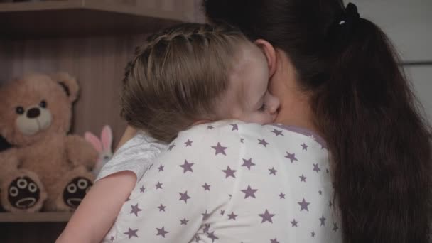Milující mladá matka objímá svou roztomilou sladkou dceru, která usne v náručí. Šťastná rodina. Zlato, dítě spí v náručí své matky. Milý, starostlivý matka a roztomilé holčička objímání v ložnici — Stock video