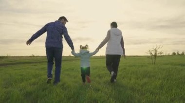 Anne, baba daha çocuk, bir kız çocuğu yeşil çimlerde koşuyor, sahada oynuyor. Mutlu aile yazın gün batımında el ele tutuşarak parkta yürür. Takım çalışması. Mutlu sağlıklı bir çocukluk