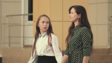 Mutlu aile anne ve çocuğu, güneş ışığında el ele tutuşarak okula giderler. Anne ve kız öğrenci bir sırt çantasıyla gidip annelerinin elini tutuyor. okul eğitimi kavramı.