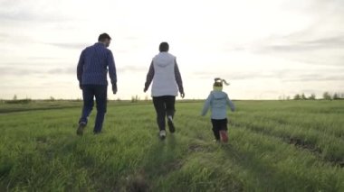 Ebeveynler ve kızları yeşil çimlerde koşuyorlar. Aile tatili. Baharda mutlu aile hafta sonları. Mutlu aile gün batımında parkta oynar ve koşar. Aile takım çalışması. Çocuklar, aileler koşuyor..