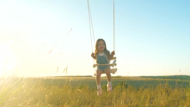 Šťastné dítě, dcera letí jako letadlo na houpačce na slunci. Máma třese dcerou na houpačce pod stromem v parku. Šťastnou rodinu. Děvčátko se směje, raduje se na hřišti. Rodinná dovolená — Stock video