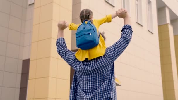 Gelukkige familie, vader en kind gaan naar school. Kleine dochter zit op de schouders van papa, ze gaan samen naar school. Voorschools onderwijs. Schatje, ga studeren. Familie uitje na school — Stockvideo