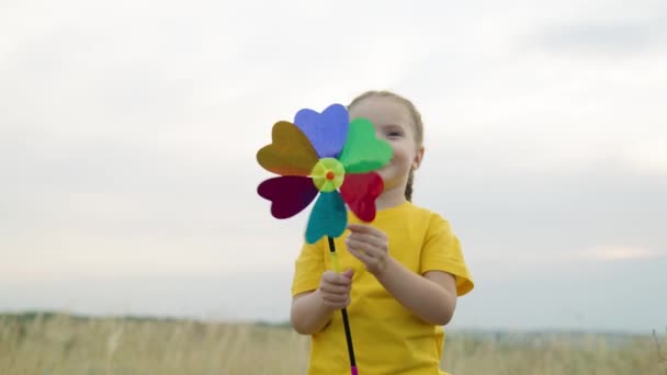 Gelukkige kind spelen leuke windmolen draaitafel buiten. Familie vakantie. Meisje speelt met een speeltje veelkleurige draaitafel in haar hand in de herfst in het park. Gelukkige familie rust uit op een weekend in de natuur. — Stockvideo