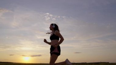 Yazın şafak vakti parkta koşan, kulaklıkla müzik dinleyen mutlu bir kadın. Sağlıklı koşu ve açık hava egzersiz konsepti. Antrenman koşusu. İnternet olmadan müzik dinlemek ve spor yapmak.