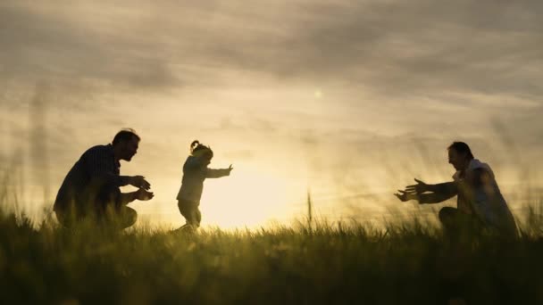 Mutlu aile gün batımında parkta oynuyor. Kızı güneşte babasından annesine koşuyor. Mutlu aile ve çocukluk kavramı. Baharda çimlerin üzerinde aile hafta sonu. Doğada küçük bir çocukla yürümek. — Stok video