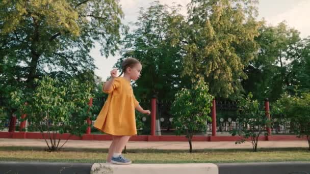 Niña pequeña camina en el parque de verano. Familia feliz, infancia alegre. El niño juega, aprende a mantener el equilibrio. Mi hija está jugando en el patio. Un niño camina por la ciudad en la calle. Sueños de infancia — Vídeos de Stock