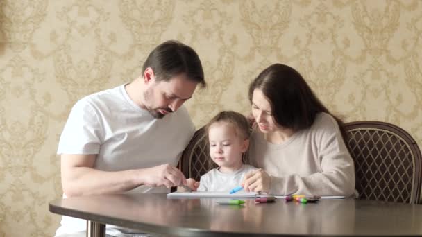 Anne, baba, çocuk, kız çocukları evde resim çiziyor. Küçük bir kız, ailesiyle birlikte hayal gücünü kullanarak renkli kalemlerle resim çiziyor. Anne ve anne evde birlikte oynuyorlar. Aile eğitimi — Stok video