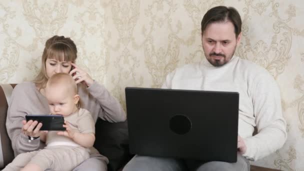 Una familia con un niño está trabajando en casa en la computadora y usando el teléfono, un niño con un teléfono inteligente en sus manos. Trabajar desde casa con portátil durante la cuarentena. Ministerio del Interior, hijo, los padres son autónomos. — Vídeos de Stock