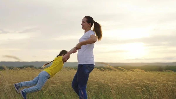 Mamá gira sus manos alrededor de su hija feliz en el parque al atardecer. Madre, hijo, jueguen juntos, ríanse, regocíjense. Feliz viaje familiar. El bebé está en brazos de los padres. Mamá y su hija familia felices vacaciones — Foto de Stock