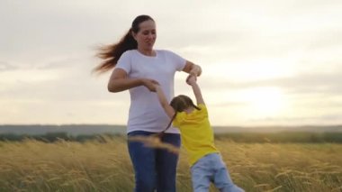 Anne gün batımında mutlu kızının etrafında döner. Anne, çocuk, birlikte oynayın, gülün, sevinin. Mutlu aile gezileri. Bebek ebeveynlerin kollarında. Anne ve kızının tatilleri kutlu olsun.