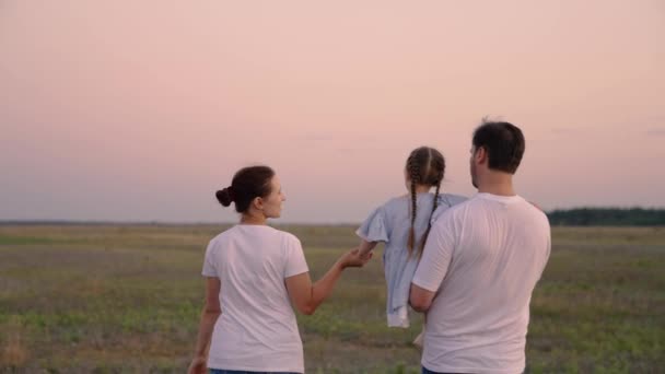 Mamá, papá e hija están caminando, el bebé se sienta en brazos de papás y lo abraza. Feliz paseo familiar en el parque en primavera al atardecer. Feliz infancia sana. Fin de semana familiar. padres e hijos — Vídeos de Stock