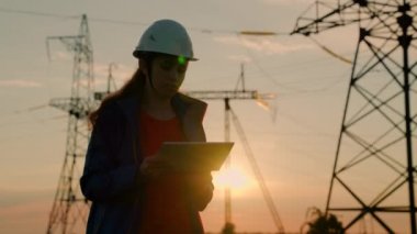 Çevre dostu elektrik. Kadın elektrik tedarik şirketi çalışanı dışarıda çalışıyor. Modern teknolojiler. Koruyucu miğferdeki kadın güç mühendisi dijital tablet kullanarak güç hattını kontrol ediyor..