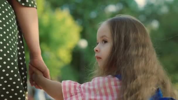 A child, a schoolboy, walks down street with a backpack, holding his mothers hand. Happy family, mother and daughter go to school together holding hands. Preschool education. Baby, girl goes to study — Stock Video