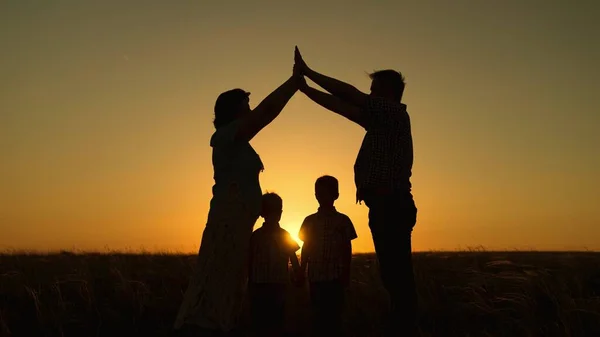 Glad familj drömmer om sitt eget hem i parken på sommaren i solsken. Barn mamma och pappa leker tillsammans bygga hus med händerna, siluett vid solnedgången. Föräldrars omvårdnad av barn — Stockfoto