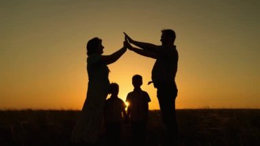 Mutlu aile hayalleri yazları parktaki evlerinin güneşli olması. Çocuklar, anne ve baba birlikte oynuyorlar. Elleriyle ev yapıyorlar. Gün batımında siluet yapıyorlar. Ebeveynlerin çocuklarına bakmak.