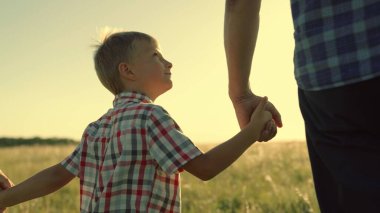 Oğlu, babası, annesi güneşin altında parkta el ele yürür. Parktaki insanlar. Mutlu aile yürüyüşleri, dışarıda baba oğul. Mutlu aile çocukluk hayali kavramı. Ebeveynler, çocuklar. Oğul baba birlikte anne