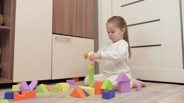 Çocuk bir aile evi inşa ediyor. Çocukların gelişimi için eğitici oyunlar. Bir çocuğa oyun oynayarak öğretmek. Mutlu bir aile. Kız, yerdeki çocuk odasında renkli küplerle oynuyor..