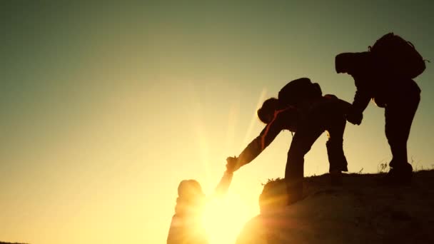 Las siluetas de los escaladores estiran sus manos entre sí, subiendo a la cima de la colina. Los viajeros suben uno tras otro en la roca. Trabajo en equipo de gente de negocios. Un equipo de empresarios va a ganar. — Vídeos de Stock