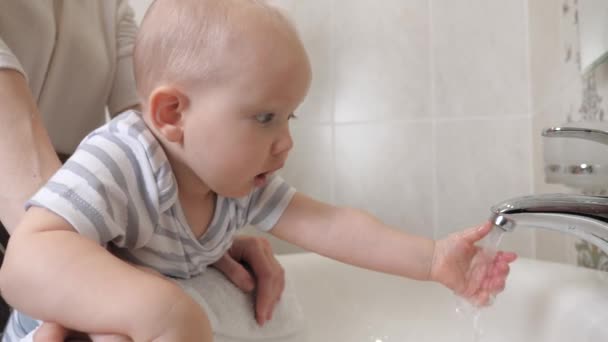 Een moeder helpt haar kind thuis hun handen te wassen. De jongen leert zijn handen zelf te wassen. Een gelukkig gezin. Water spelen met het kind. Een klein kind wast zijn handen met zijn moeder in de badkamer boven wastafel. — Stockvideo