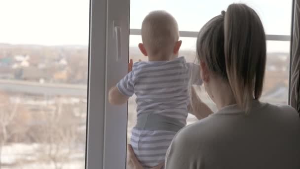 Mamma, barn, dotter leker och tittar ut genom fönstret på gatan, mamma uppfostrar små barn hemma. Baby och mamma. En lycklig familj. Grabben, grabben, den unga modern väntar på pappa tillsammans. Hemundervisning — Stockvideo