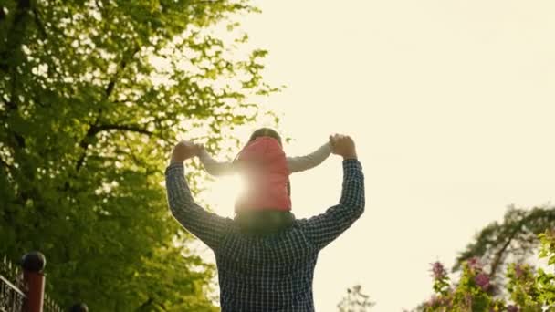 Papà porta il bambino sulle spalle, insieme a sua figlia sognano di volare, la famiglia cammina per strada al sole. Padre, il bambino sta giocando nel parco. Una famiglia felice, insieme. Weekend nella natura — Video Stock